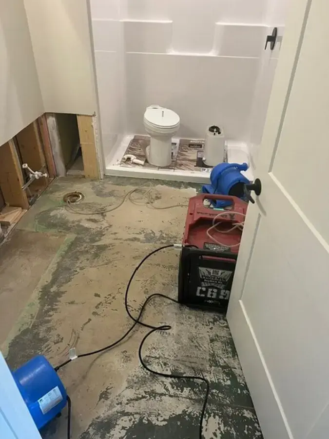Air mover and dehumidifier drying a bathroom subfloor after the flooring and tub surround were opened