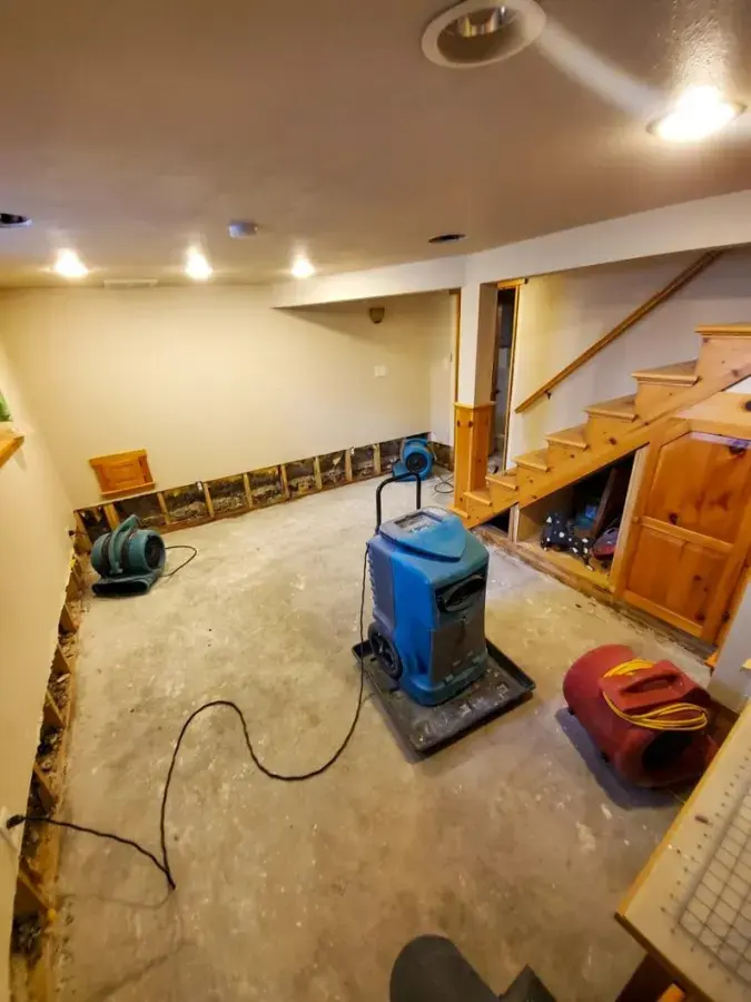 Dehumidifier and air movers drying a finished lower level beside the stairs in a Burnsville home